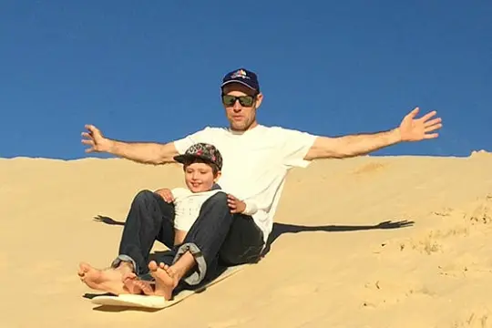 a man and a kid sand boarding down a sand dune in Port Stephens