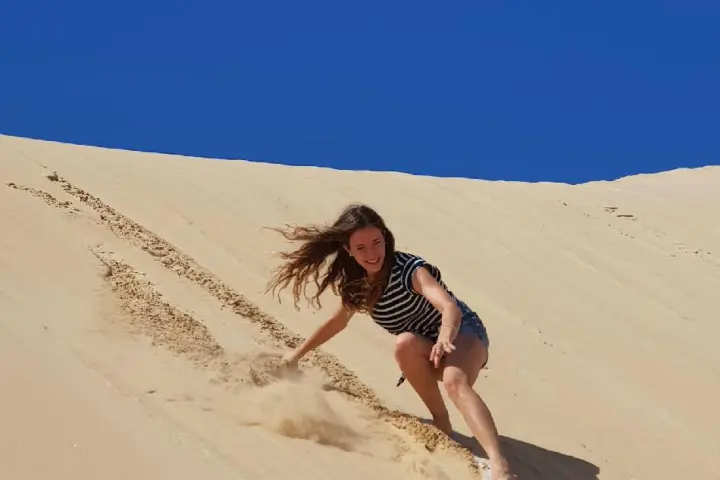 a person sand surfing down a sand dune in Port Stephens