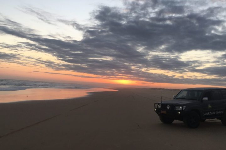 a car parked on Stockton Beach with a sunset in the background